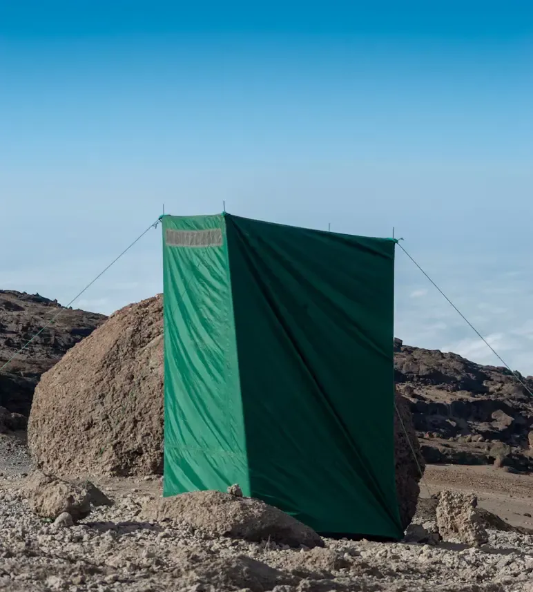 Private portable toilet tent on the rocky slopes of Mount Kilimanjaro under a clear blue sky.